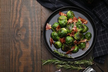 Delicious roasted Brussels sprouts, bacon and rosemary on wooden table, top view. Space for text
