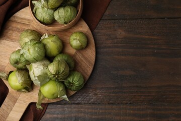 Fresh green tomatillos with husk in bowl on wooden table, top view. Space for text