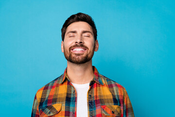 Portrait of optimistic dreamy positive guy with stubble wear plaid shirt smiling close eyes relaxing isolated on blue color background