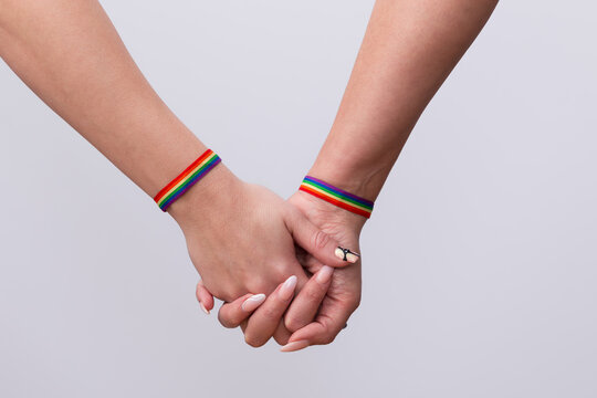 Close up of joined hands and nice manicure of a lesbian couple with rainbow flag bracelets on white background. Concept of LGTBI pride and LGTBI rights
