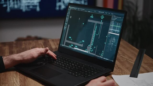 An architect is working on blueprints using a laptop. The shot shows male hands and a laptop with an engineering software program open. The project involves developing a construction plan