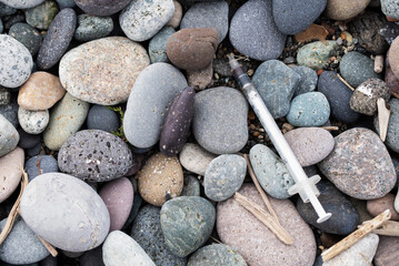 A drug addict's used syringe on a pebble beach close-up. Environmental pollution