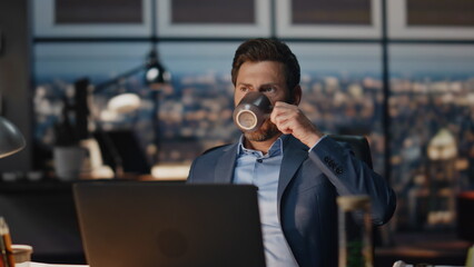 Pensive businessman drinking tea in night office closeup. Director taking break