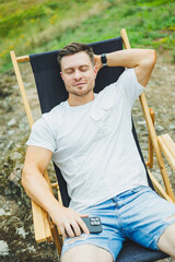 Cute smiling man on folding wooden chair sitting in nature and resting. The concept of recreation...