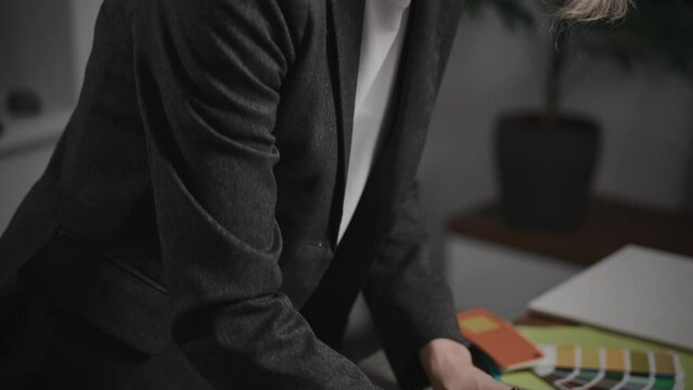 A woman interior designer is creating a mood board. The specialist is using palettes, as well as texture and material samples. The woman is working in a design studio. The office