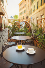A cup of coffee and juice on table, in italian street, mediterranean style. Street view of a summer terrace cafe with table and chairs. Cup of italian espresso on a table in a street cafe. Urban scene