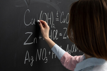 Back view of a female student writing the formula of a chemical reaction on the blackboard	