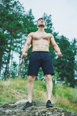 Young muscular man on the background of rocks. Athletic pumped-up man with a bare torso poses against the background of a forest rock.