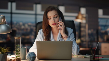 Business woman speaking smartphone at night workplace. Calling lady making notes