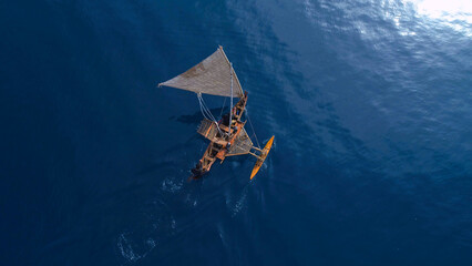 Aerial shot of a traditional Micronesian outrigger sailing canoe surrounded by blue water