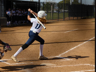 Young female Softball player playing youth sports. Swinging bat.