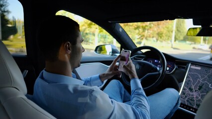 Successful businessman browsing modern smartphone while riding an autonomous self driving electric car. Male entrepreneur using phone during riding on electrical auto with autopilot at urban road - 759086728