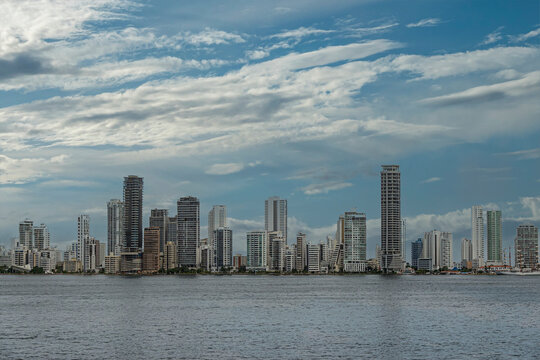 Cartagena, Colombia - July 25, 2023: Long section of east shore with apartment buildings at Bocagrande Neighborhood under blue cloudscape. Tall ship docked at Naval Base 