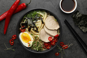 Delicious ramen with meat in bowl and ingredients on grey textured table, flat lay. Noodle soup