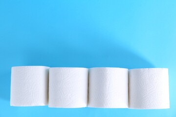 Soft toilet paper rolls on light blue background, flat lay. Space for text
