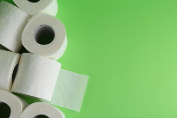 Soft toilet paper rolls on green background, flat lay. Space for text
