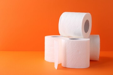 Soft toilet paper rolls on orange background, closeup. Space for text