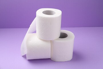 Soft toilet paper rolls on violet background, closeup