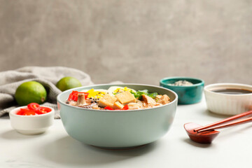 Bowl of delicious ramen, ingredients and chopsticks on white table, closeup. Noodle soup