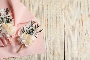 Stylish boutonnieres and pink fabric on light wooden table, top view. Space for text © New Africa