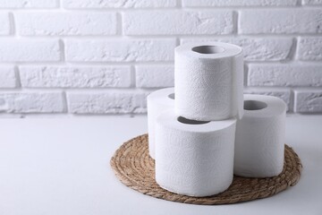 Toilet paper rolls on white table against brick wall, space for text