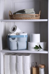 Toilet paper rolls, green leaves, towels and cotton pads on white shelves