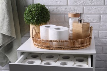 Toilet paper rolls, floral decor, dispenser and cotton pads on chest of drawers indoors