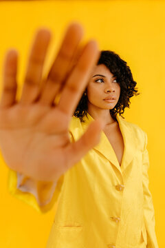 Stylish woman showing stop sign in yellow studio