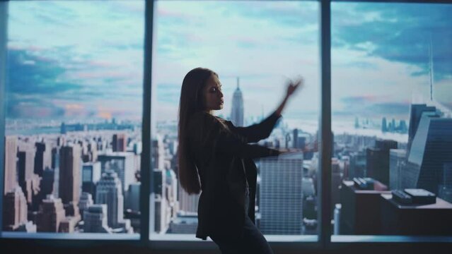Successful business woman in the office. Woman ceo hedge fund top manager dancing in front of window with morning city view.