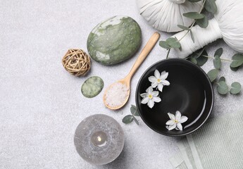 Flat lay composition with herbal massage bags, spa products and flowers on light grey table