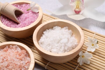 Obraz na płótnie Canvas Different types of sea salt and flowers on light table, closeup. Spa products