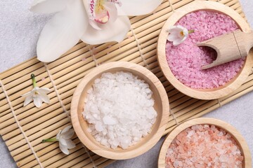 Fototapeta na wymiar Different types of sea salt and flowers on light table, flat lay. Spa products
