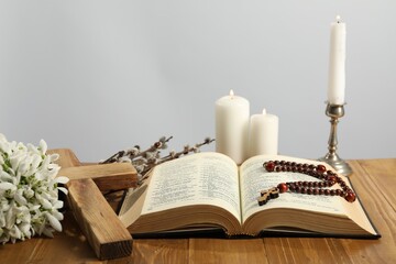 Church candles, cross, rosary beads, Bible, snowdrops and willow branches on wooden table against light background - obrazy, fototapety, plakaty