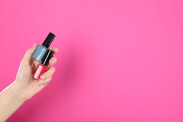 Woman holding nail polishes on pink background, closeup. Space for text