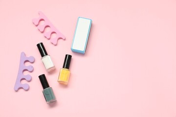 Nail polishes, toe separators and buffer on pink background, flat lay. Space for text