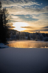 Sunset over snow-covered lake with trees, tranquil winter scene