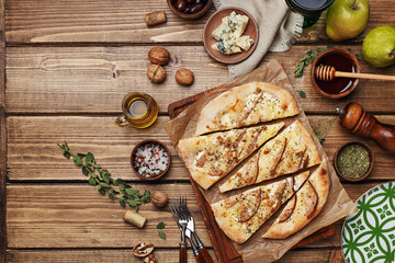 Sliced flatbread pizza with pears, blue cheese and walnut on wooden background with ingredients for cooking. Top view, flat lay, copy space. Italian food concept