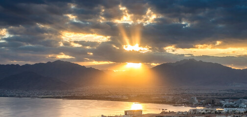 Panoramic morning view with sunbeams, Eilat (Israel) and Aqaba (Jordan) cities, and Aqaba gulf all seen from surrounding hills in Eilat- 759099781