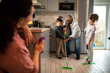Young family sweeping the kitchen floor at home