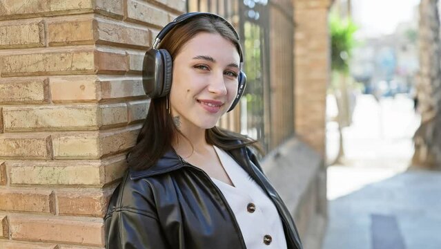 Young brunette woman wearing headphones posing in urban city street with blurred background