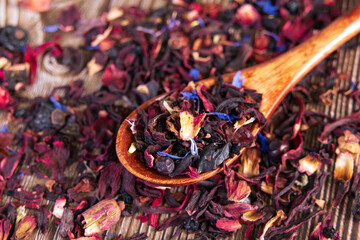 Tea mix of karkade, flowers and berries in a spoon and on the table.
