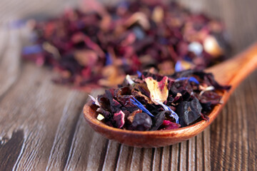 Tea mix of karkade, flowers and berries in a spoon and on the table.