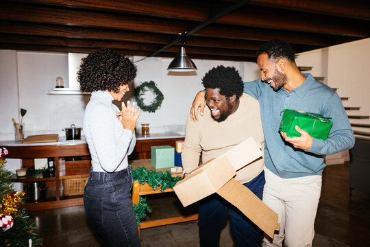 Cheerful friends opening gifts at home on christmas day Ugc