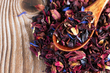 Tea mix of karkade, flowers and berries in a spoon and on the table.