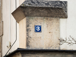 Number 3 on an exterior house wall. The metal plate is enameled and in blue color. The design very vintage and retro. The three is also a prime number and part of an address.