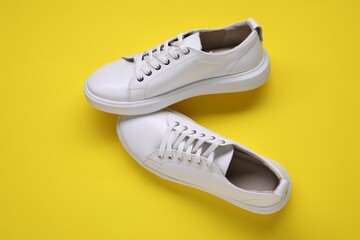 Pair of stylish white sneakers on yellow background, top view