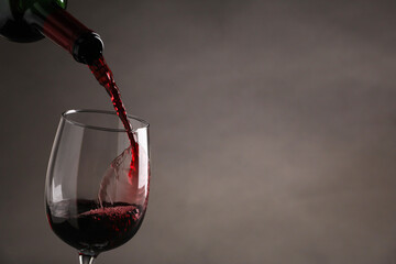 Pouring tasty red wine from bottle into glass on gray background, closeup. Space for text
