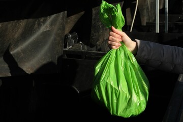 Woman throwing trash bag full of garbage in bin outdoors, closeup