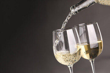 Pouring white wine into glass against grey background, closeup. Space for text