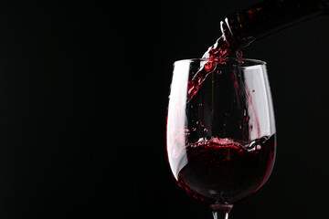 Pouring red wine into glass against black background, closeup. Space for text